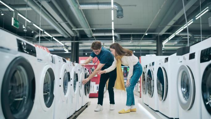 时尚女性在选择洗衣机时与家电商店顾问互动。年轻顾客探索洗衣设备选择。现代零售商店里的顾客