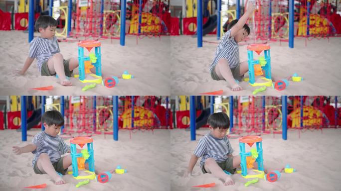 一个小男孩正在把沙子倒进漏斗里，独自一人在沙坑里旋转着轮子。