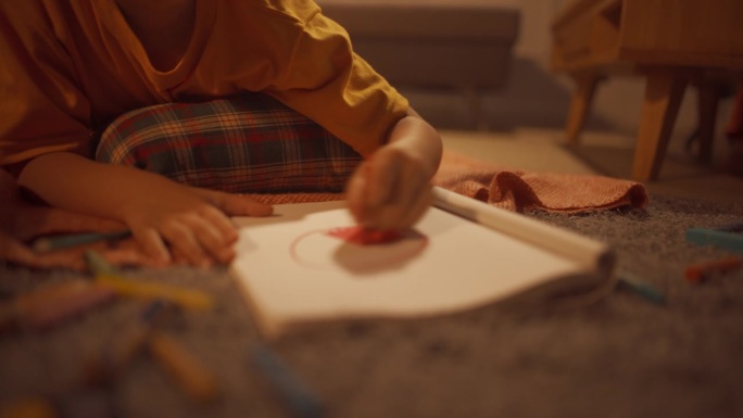 可爱的韩国男孩躺在地板上，用铅笔和钢笔在笔记本上画画的特写。艺术儿童画一个橙色的圆形在家里舒适的正宗