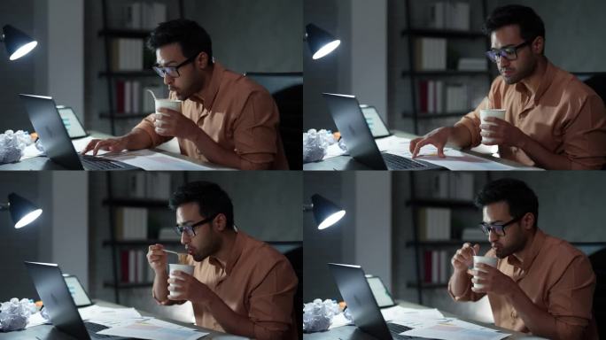 一名亚洲年轻男子在加班期间一边做项目计划，一边坐在办公桌前吃泡面。