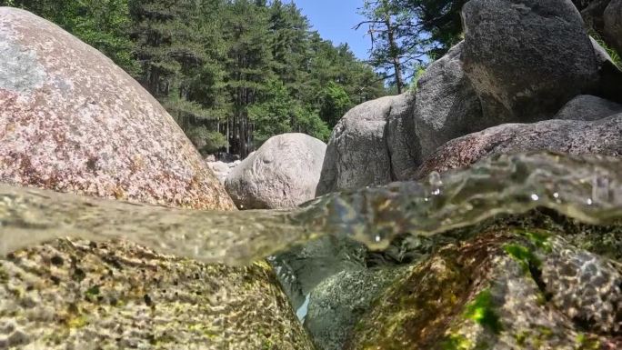 水流在石头之间流动，形成小瀑布和浴池。流着清澈的水和气泡。半水下慢动作镜头