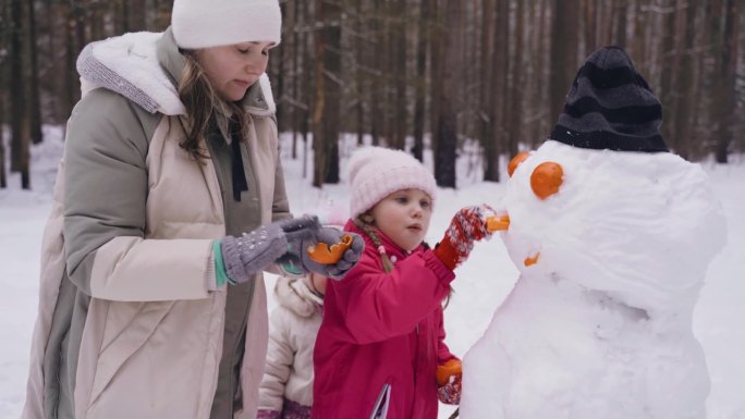 女孩们和她们的妈妈用橘子皮做雪人的牙齿。