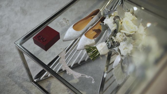新娘的白鞋，结婚戒指和新娘的珠宝放在酒店房间的玻璃桌上，慢镜头。