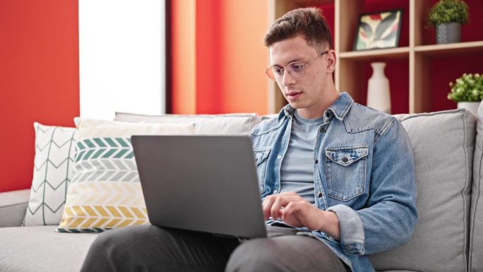 年轻的西班牙裔男子坐在沙发上使用笔记本电脑，神情紧张