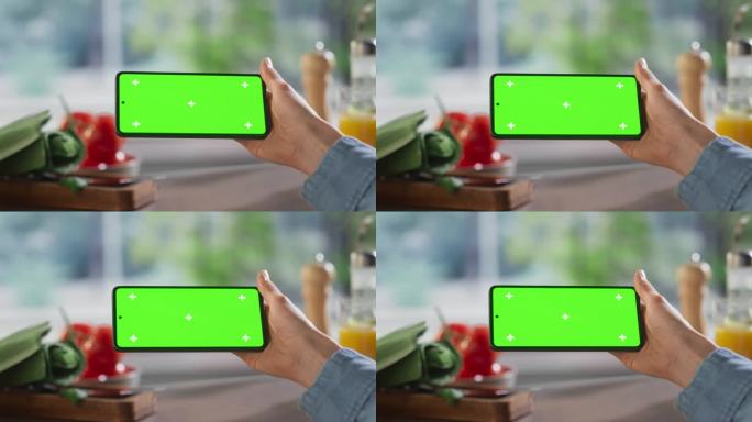 静态拍摄的匿名妇女使用智能手机与模拟绿色屏幕Chromakey显示在厨房餐桌上的食物配料。女性在流媒