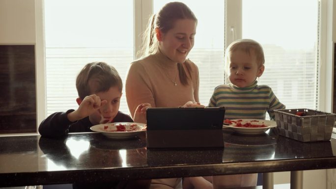 两个可爱的男孩一边喝汤一边看平板电脑视频。家常菜，在家做饭，孩子健康营养
