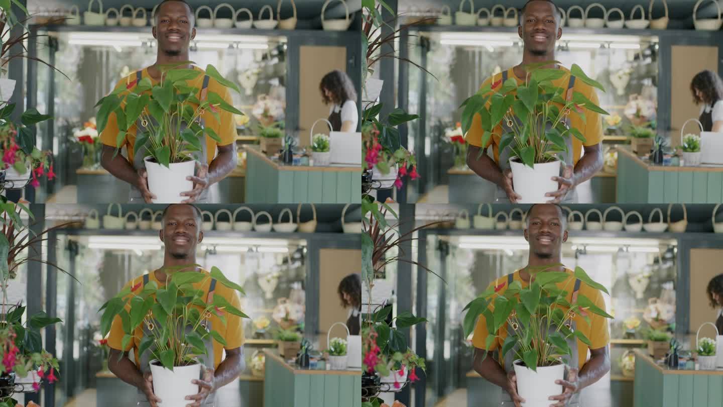 穿着围裙的非裔美国人站在花店卖绿色植物的肖像，微笑着看着镜头