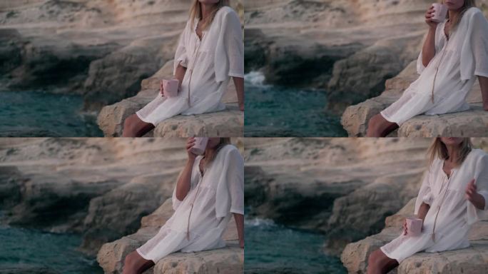 右边是一个无法辨认的女人，她拿着茶杯坐在地中海的岩石上。高加索女游客端着咖啡在塞浦路斯欣赏日落。