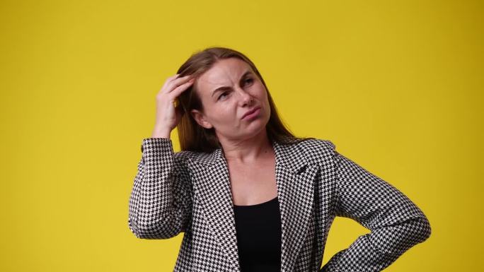 一段4k视频显示，一个女人在黄色背景下抓耳挠腮，思考着什么。