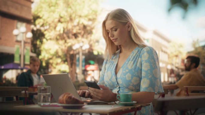 一个年轻的白人女性使用智能手机和笔记本电脑工作的肖像。远程工作专家在户外城市咖啡馆多任务公司管理任务