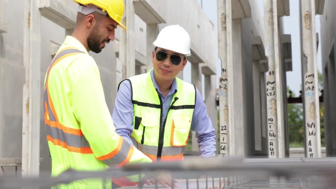 建筑和建筑工人，拉丁裔和亚洲男性，戴安全安全帽头盔，在预制混凝土墙制造中为混凝土板加固用钢丝网工作