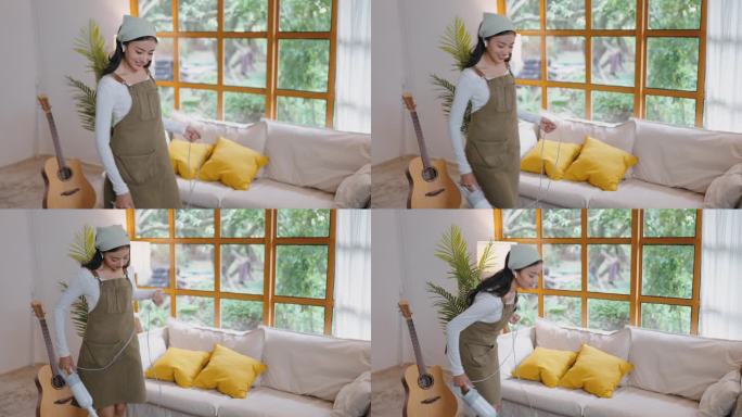 亚洲女性做家务在家里吸尘，在家里打扫房间时戴着耳机跳舞唱歌听音乐