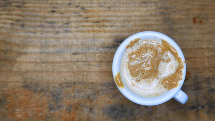 一杯美丽的奶油咖啡:将沸水倒在一杯奶油咖啡上。用勺子搅拌咖啡。桌上有一杯咖啡。表格，俯视图。热气从热