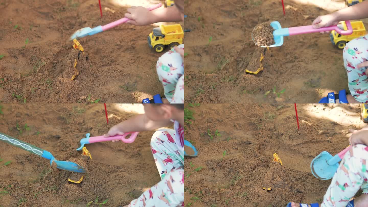 一个亚洲男孩用玩具挖掘机和自卸卡车玩和挖沙子。