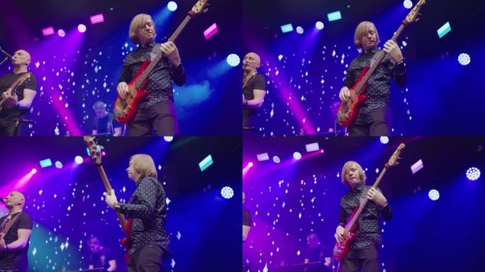 在蓝色和粉红色的聚光灯下，贝斯吉他手在音乐会的舞台上表演。慢动作