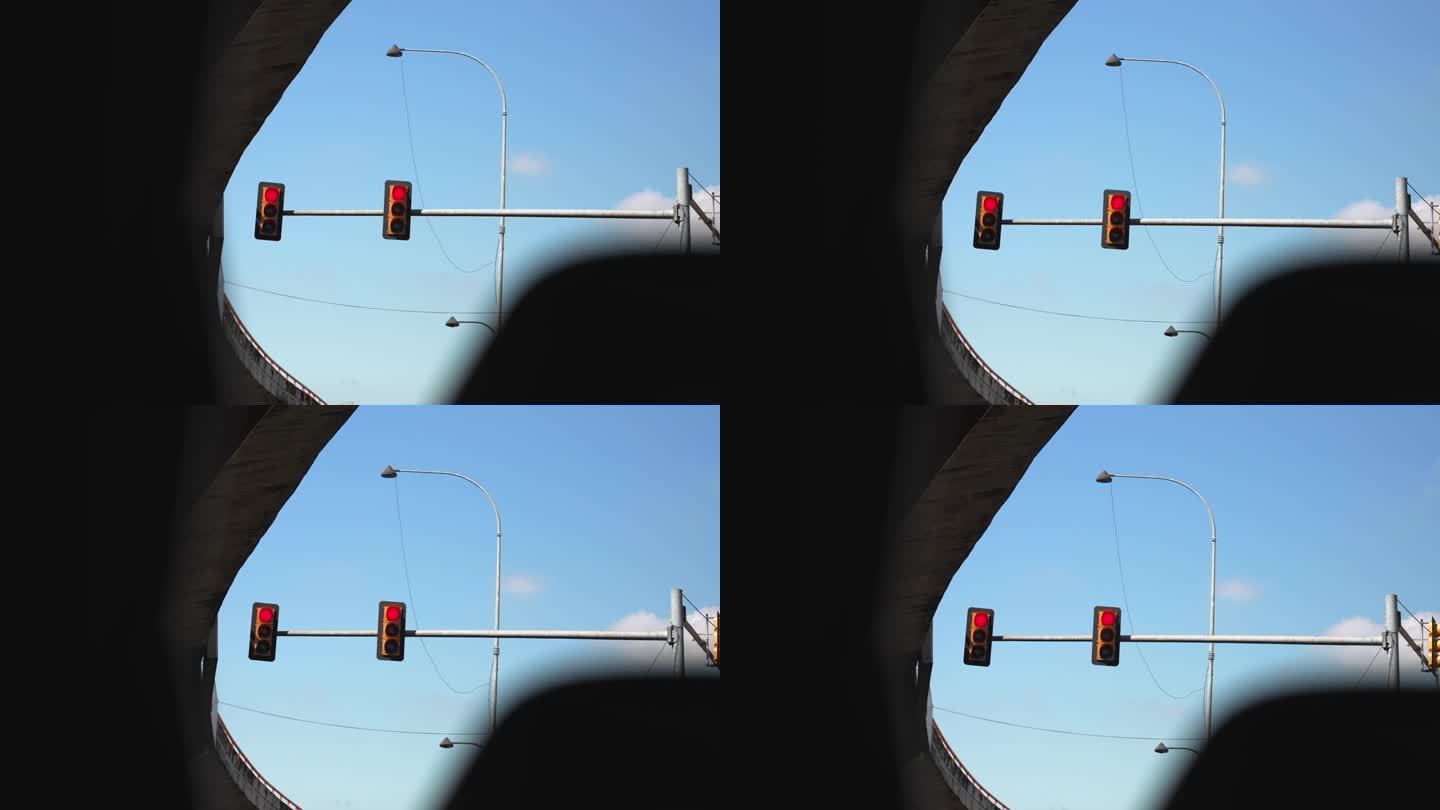 从汽车上看十字路口桥下的柱子上挂着两个交通灯。红色的光和蓝色的天空为背景