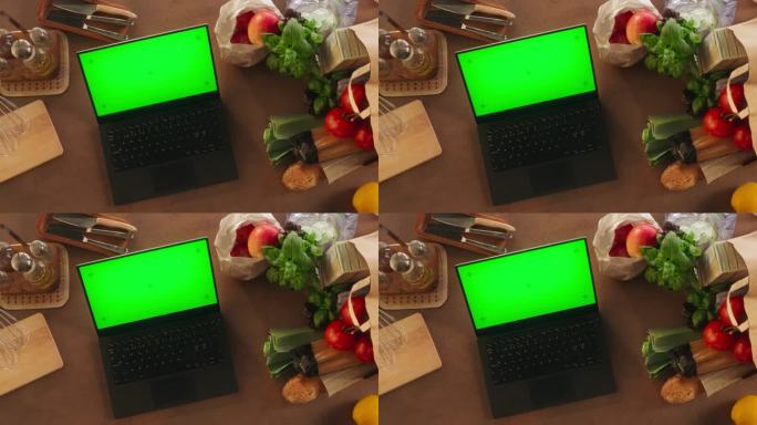 一台笔记本电脑的俯视图，配有模拟绿屏Chromakey显示屏和运动追踪器，它站在厨房的木桌上，旁边是