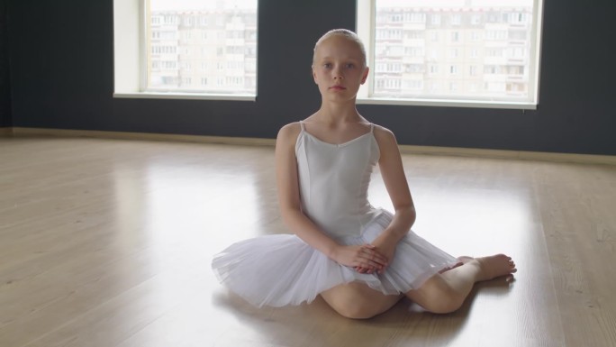 芭蕾舞学校的小舞者坐在地板上，看着镜头