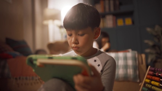 聪明男孩在儿童房使用数码平板电脑的肖像，背景是他的小妹妹正在画画。聪明的韩国孩子用科技教育、学习和思