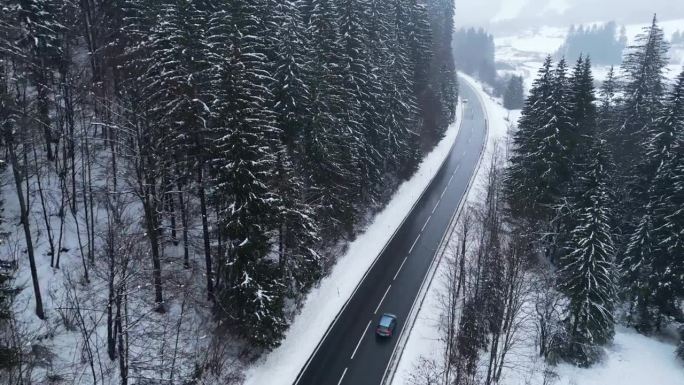 航拍的车辆沿着斯洛文尼亚被雪覆盖的树木在柏油路上行驶