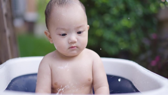 小男孩玩得很开心，把水溅到婴儿浴盆上。