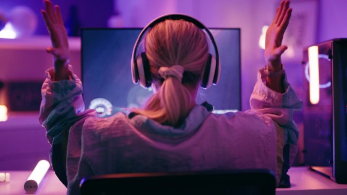 女人、游戏玩家和电脑在夜晚用霓虹灯庆祝胜利、胜利或成就。女游戏专业人士在家里庆祝电子竞技胜利的后视图