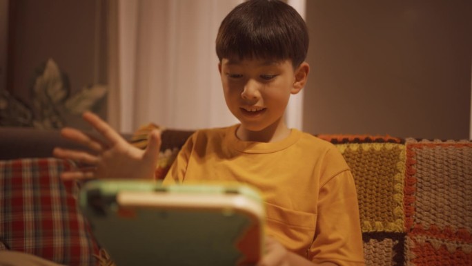 一个快乐兴奋的孩子在家里的客厅里使用平板电脑的中等肖像。聪明的男孩在一个教育游戏中获胜，达到高分，庆