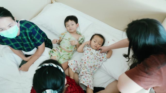 一个亚洲家庭在医院安慰和玩耍两个生病的孩子。健康的生活方式。流感病毒A。