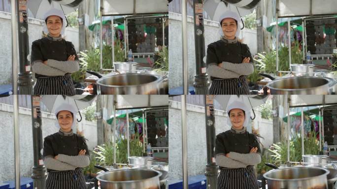身穿黑色围裙的亚洲街头小吃女厨师站在她的店里，双臂交叉。
