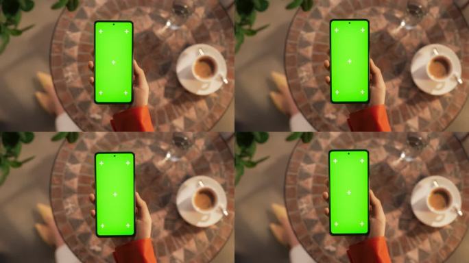 一个女人坐在咖啡桌旁，拿着智能手机，看着一个绿色的Chromakey模拟显示屏。视频模板与占位符的数