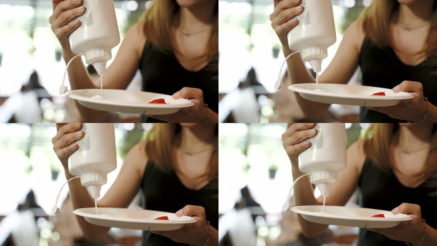 特写年轻女子手持水彩瓶，正用手把白色的瓶子挤进纸盘，把原色挤进纸盘，如果要用其他颜色，就用原色。