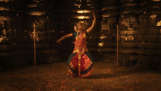 迷人的慢动作肖像印度女舞者表达自己通过迷人的民间舞蹈编排在一个古老的寺庙。她穿着传统服装，跳着Bha