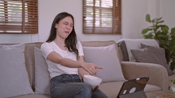 亚洲女性吃零食和看搞笑电影在便携式平板电脑上，不健康的生活方式理念。
