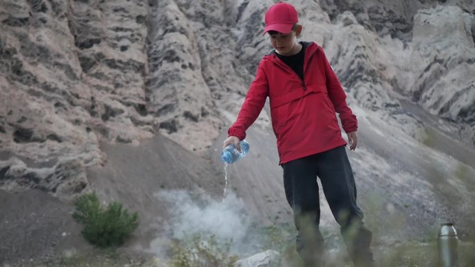 一个十几岁的男孩在山上野餐后，从塑料瓶里倒水，点燃了篝火。孩子把水倒在火上，把瓶子倒着拿。防火措施