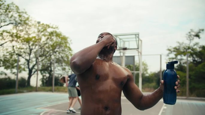 一位皮肤黝黑的男子在打完篮球后，用特制的瓶子把水倒在头上降温，然后在篮球场上喊出他的战斗口号