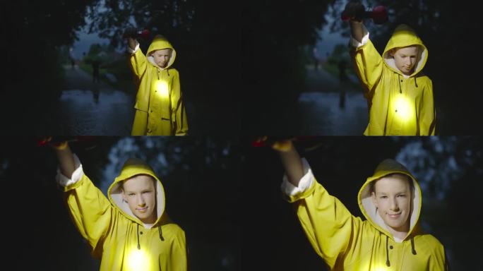 穿着黄色雨衣的微笑小男孩在被水淹没的道路上拿着手电筒