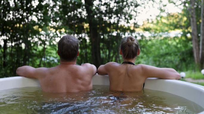 一对年轻夫妇在森林度假胜地的户外热水浴池里放松。水疗自然护理，浪漫之旅