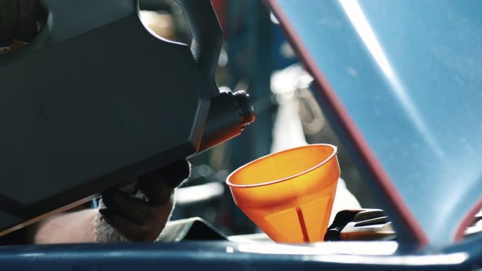 资深机械师在车库里给发动机罩下的发动机注入机油。