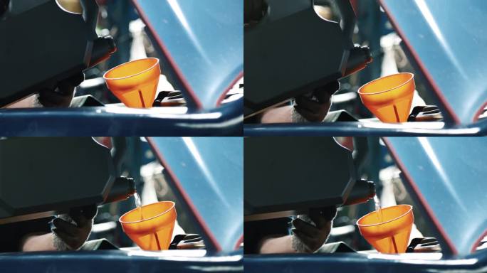 资深机械师在车库里给发动机罩下的发动机注入机油。