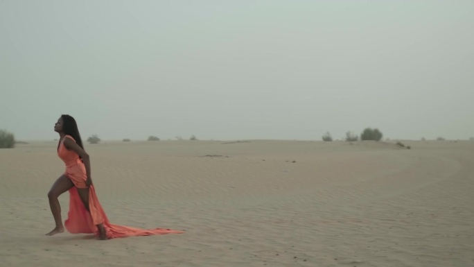 黑发的年轻女子赤脚走在沙漠的沙滩上，衣服在风中飘动