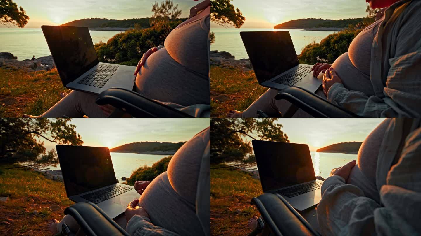 孕妇在日落时分摸着肚子用笔记本电脑