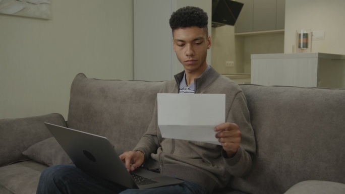 看着笔记本电脑处理文件的黑人。30多岁的企业家在家办公室管理文件、发票、税单。