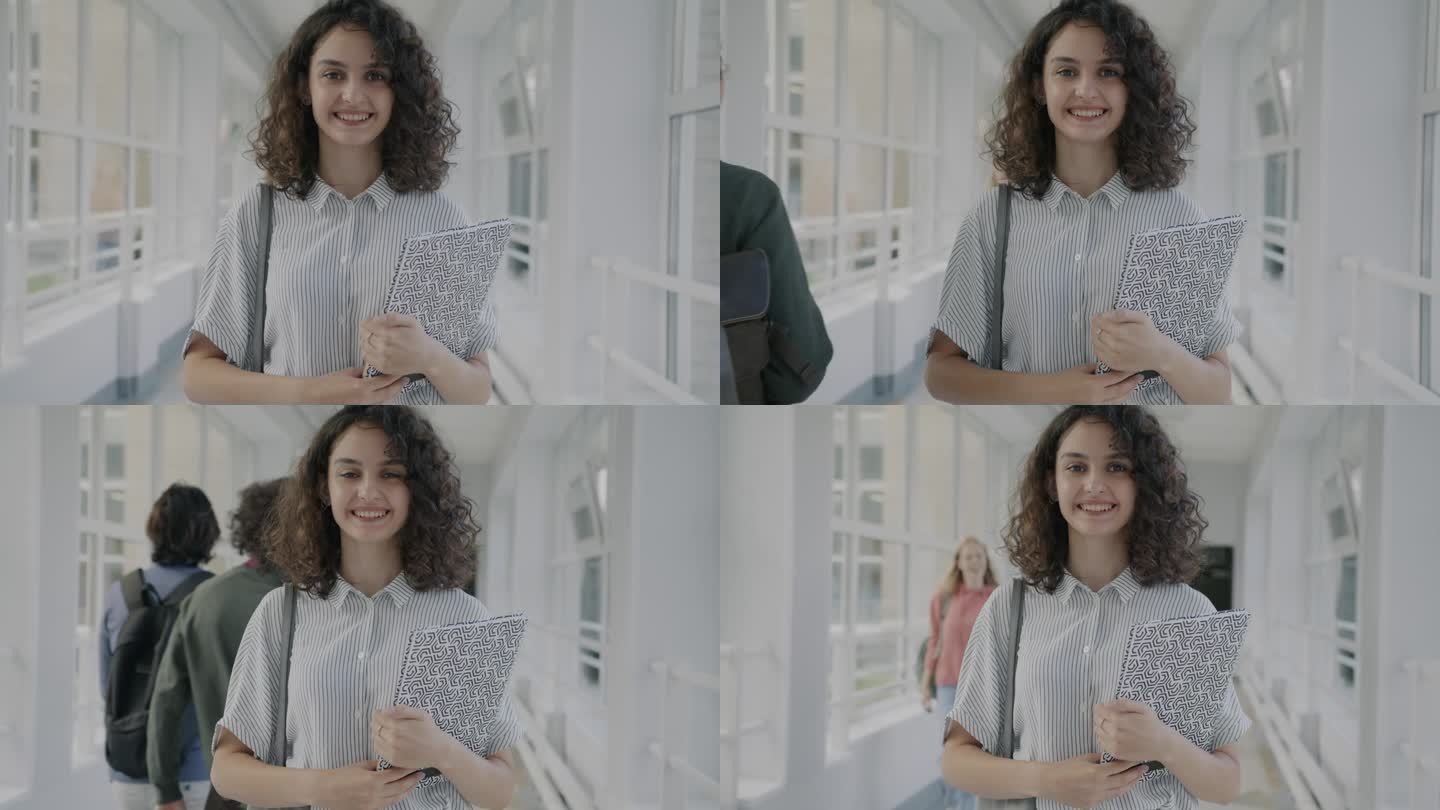 一个快乐的女孩站在现代大学的大厅里，拿着教科书，微笑着看着学生们走过