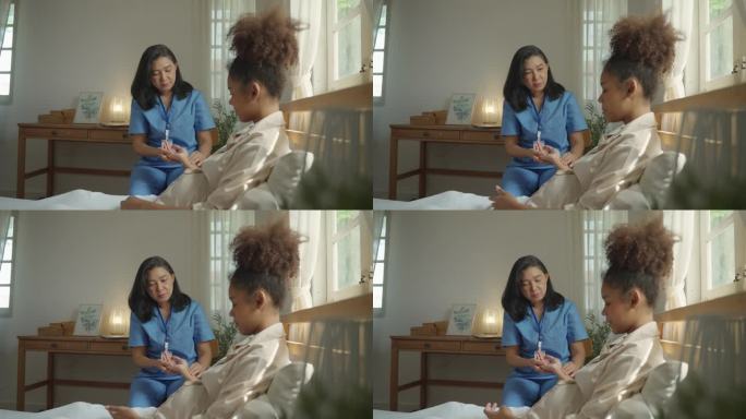 穿着蓝袍子的亚洲女家庭护士在卧室里听着一个黑人孕妇的心跳。孕妇由家庭护士每月随访一次(侧面图)