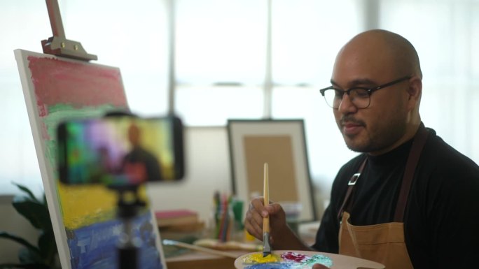 艺术家在网上直播课堂上用画笔在画布上绘画，通过智能手机进行艺术和油画。美术老师在线教授创意绘画课供学