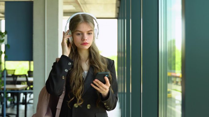 一名女学生在大学课间休息时，戴着耳机听播客电子书歌曲，用手机选择音轨