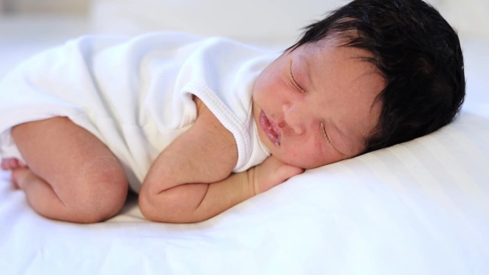一个刚出生的非洲裔黑人婴儿趴在地上睡得很香，一个皮肤黝黑的小婴儿躺在卧室的床上