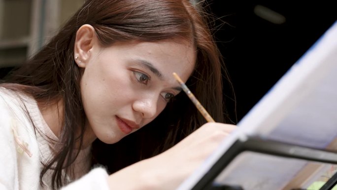 亚洲少女的脸部特写。带着坚定的目光，打算用画笔在白布上画画，十几岁的女孩喜欢在假期做一些事情。练习绘