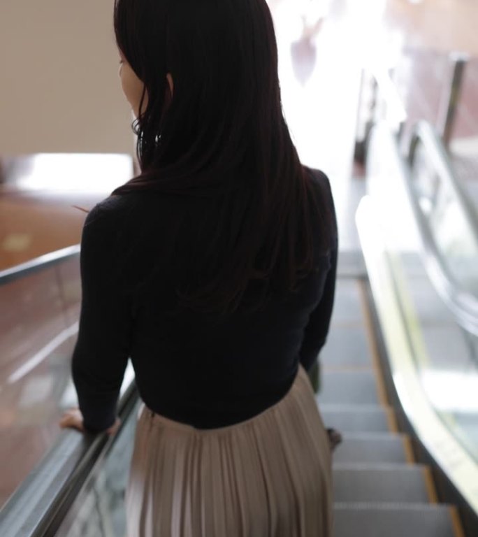 女商人在机场自动扶梯上往下走的后视图