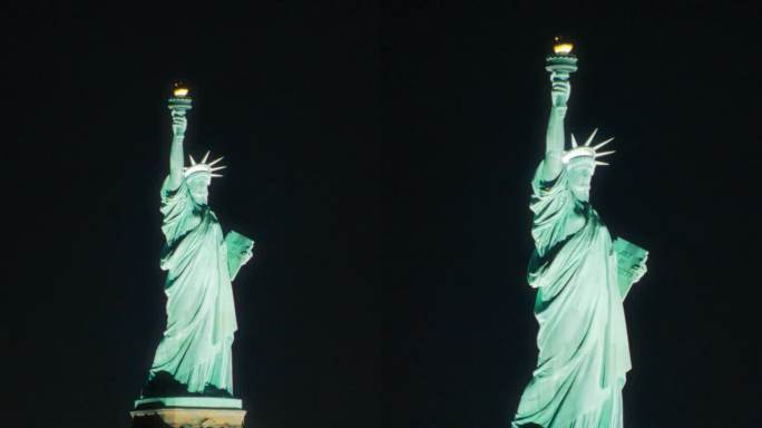 垂直屏幕:环绕自由女神像的空中飞行。直升机拍摄的美丽夜晚的爱国纪念碑。带着灯光的渡船载着游客往返于曼